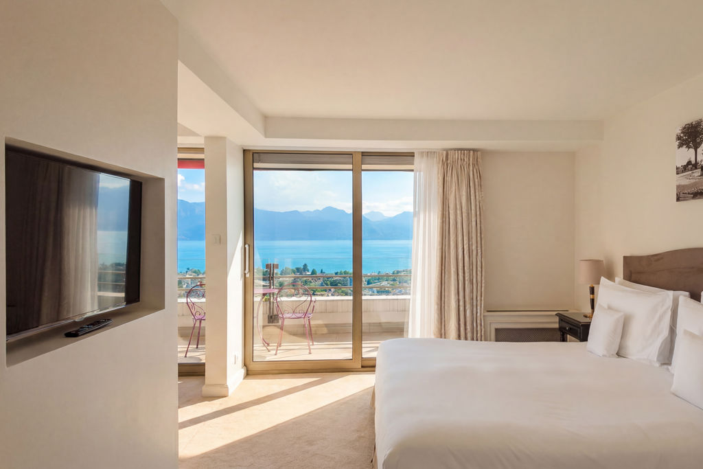 Corner Suite Lake du Lausanne Palace, hôtel 5 étoiles au cœur de Lausanne, avec chambre élégante ouverte sur un vaste balcon privatif offrant une vue panoramique sur le lac Léman, les Alpes suisses et les toits de Lausanne. Une suite de 80 m² idéale pour un séjour romantique, un voyage d'affaires ou une escapade d'exception en Suisse.